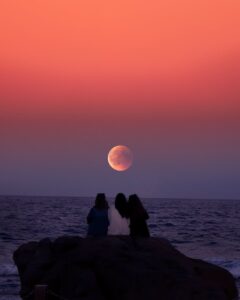 three women sitting on rock infront of ocean