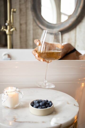 woman taking wineglass from round table in bathroom